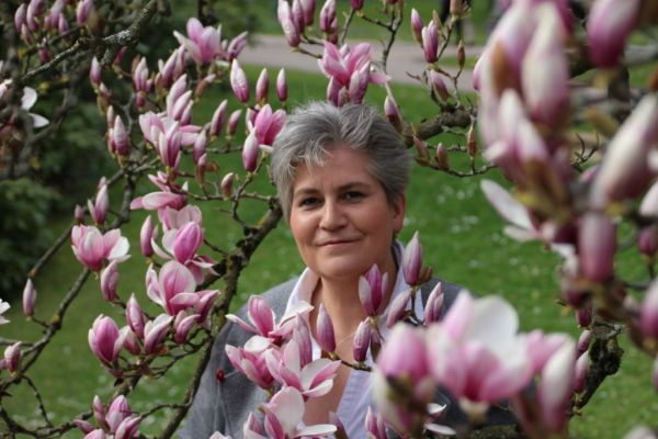 Sybille Schobel, Heilpraktikerin in Wiesbaden, fotografiert zwischen Magnolienblüten im Park