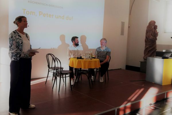 Tom Klose und Peter Post am Küchentisch. Daneben die Moderatorin Tina Tunali